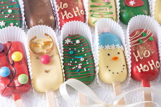 Christmas dessert. Sweet food. Cheesecake on a stick in the shape of ice cream. Children's treat in winter. Candy Christmas tree, snowman, deer and Santa Claus. Gingerbread cookies background.