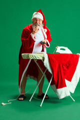 Full length portrait of funny Santa Claus holding remote control while ironing his favorite dress...