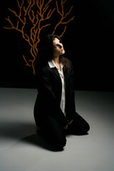 A stylish girl poses in a black suit and white shirt in a professional photo studio with a light wood pattern. Fashion shoot concept