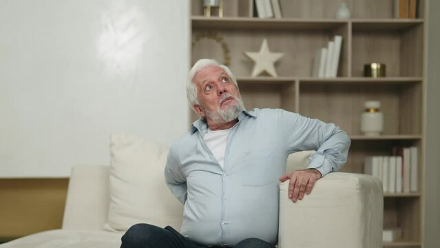 Senior man tries to stand from armchair. Elderly male suffering atherosclerosis, arthritis, osteoporosis disease. Health problems in old age, stiffness of movements, painful sensations in lower back.