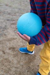 砂場でドッジボールのボールを持つ小学生低学年の男の子。遊び、スポーツ、球技