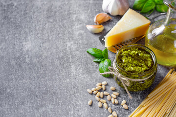 Homemade pesto sauce in small glass jar and ingredients for pasta on gray concrete background with copy space. Traditional Italian cuisine, recipe, restaurant menu