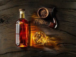 Glass of whiskey, whiskey bottle and tobacco pipe on old wooden table. Top view.