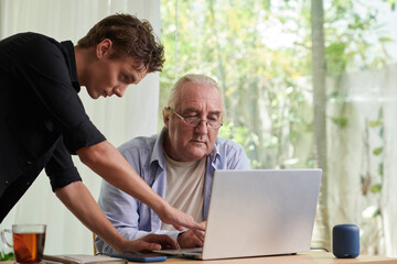 Young man showing senior father how to use laptop for communication with family
