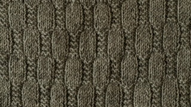 Video of fragment of gray knitted sweater with pattern. Background with knitted leaf shape, knitting pattern with cables. Top view, close-up. Handmade knitting wool or cotton fabric texture. 