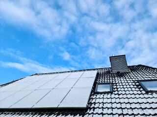 Snow covered solar panels producing clean energy on a roof of a residential house.