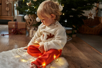 Toddler sitting on floor and playing with Christmas lights