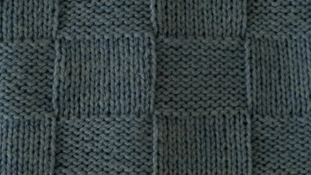 Video of fragment of knitted sweater with pattern. Top view, close-up. Handmade knitting wool or cotton fabric texture. Unusual abstract knitted chess pattern background texture. 