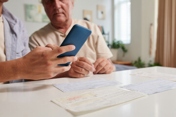 Closeup image of young man showing grandfather how pay bills online via mobile app