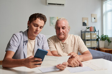 Young man paying utility bills of his grandfather via mobile app