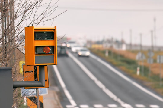 A radar-equipped speed camera monitors the traffic on a road, flashing a yellow light when it catches a car exceeding the speed limit, and using technology to identify the vehicle and enforce the law.