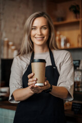 A barista in a coffee shop presents a recyclable takeaway coffee cup, highlighting eco-conscious service