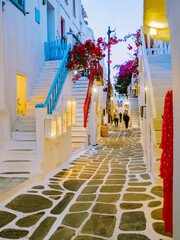 Mykonos Greece in the evening, colorful streets of the old town of Mykonos, Traditional narrow street with blue doors and white walls and street lanterns, shopping street, Mykonos town Greece - obrazy, fototapety, plakaty