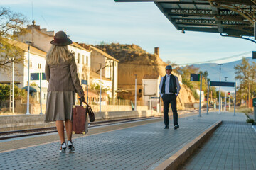 A woman is walking along the platform with her suitcase and sees a man in front of her.