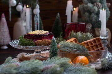 New Year's dinner with herring salad under a fur coat by candlelight. Festive table setting with tangerines and decorated with fluffy spruce and cones