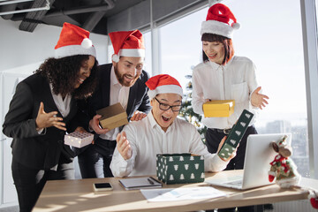 Secret Santa. Smiling Asian businessman in Santa hat unpacks a Christmas present from...
