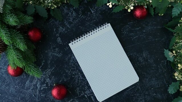 top view of female hands writing the words 2024 Goals in a notepad. Background with New Year tree and Christmas decorations. Flat lay