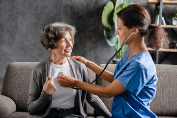 Smiling caregiver nurse listening to elderly patient grandmother heart lungs with stethoscope...