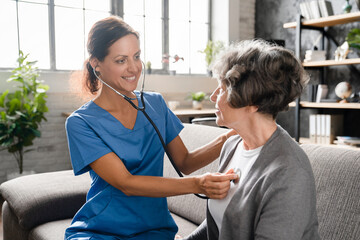 Closeup photo of smiling caregiver nurse listening to elderly patient grandmother heart lungs with...