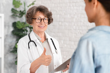 Senior female doctor gynecologist showing thumb up, telling good positive news about successful...