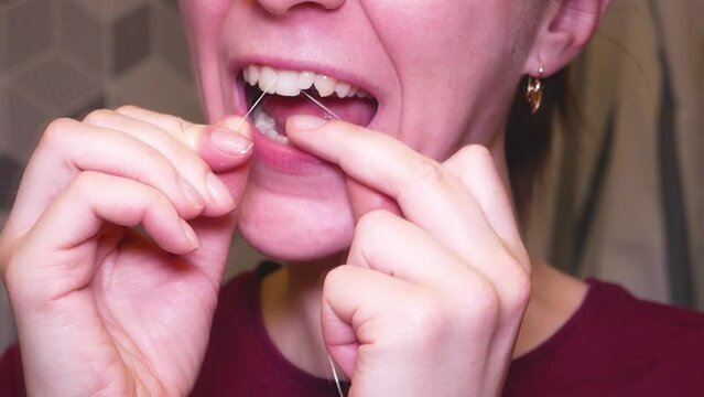 A young woman in the bathroom uses dental floss to clean crooked teeth
