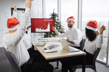 Successful team of multiethnic business people in Santa hats raising hands and screaming with...
