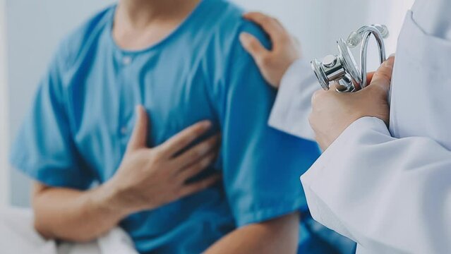 Senior doctor and young male patient who lie on the bed while checking pulse, consult and explain with nurse taking note and supporting in hospital wards.