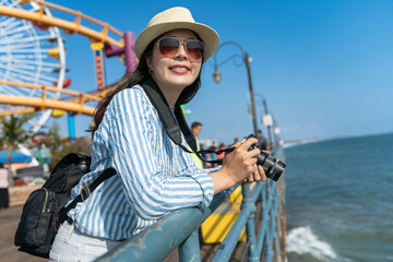 happy asian Japanese female photographer enjoying ocean scenery and california sun at waterfront amusement park of santa monica pier in united states
