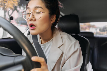 Front view of Asian Thai woman asleep and sleepy, closing eyes while driving a car on road, insurance concept.