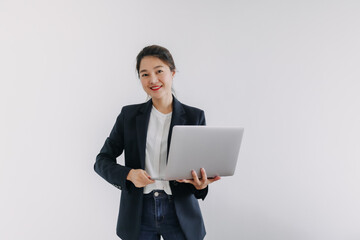Asian Thai woman wear blazer suit, smiling looking at camera and holding laptop, presenting notebook with happy face, standing isolated over white background wall.