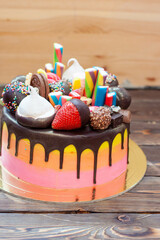 Colorful richly decorated gradient pink cake with sweets, popsicles, lollipops, jelly, strawberries and cupcakes on rustic background