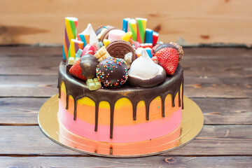 Colorful richly decorated gradient pink cake with sweets, popsicles, lollipops, jelly, strawberries and cupcakes on rustic background