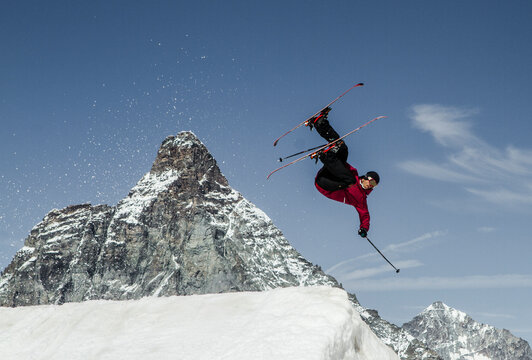 Anonymous carefree man skiing and jumping on snowy mountain while enjoying winter day at Swiss Alps