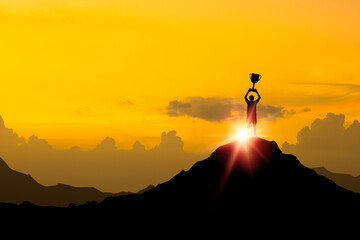 Silhouette businessman standing on top of mountain and holding a trophy with over sunlight for leadership business winner successful and achieve objective target concept. - obrazy, fototapety, plakaty