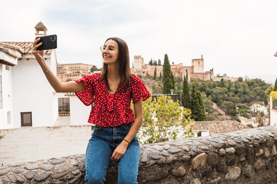 Smiling tourist taking selfie with cellphone against Alcazaba in town