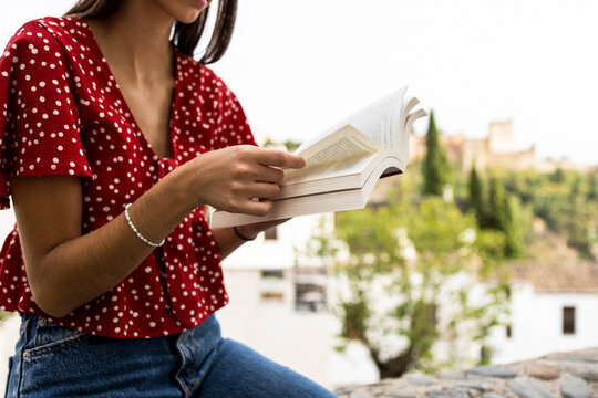 Anonymous female tourist sitting on retaining wall while reading book against Alcazaba fortress