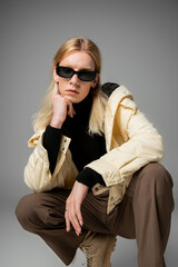 appealing androgynous person in stylish outfit with sunglasses squatting with fist under chin