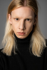 vertical shot of good looking young non binary person in black turtleneck posing on gray backdrop