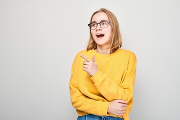 Young blond girl in yellow casual pointing finger aside, demonstrating empty space for product or...