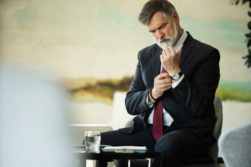 elegant mature fashion man looking at his cufflinks while fixing them