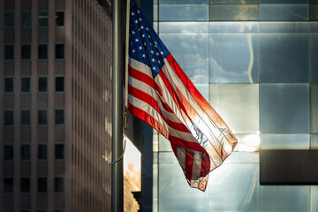 American flag waving in the wind on the pole in front of large windows and buildings of Lower...