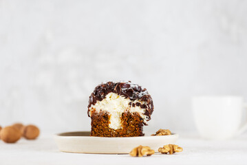 Carrot cake with vanilla cream cheese, chocolate and walnuts and cup of tea on a light background.