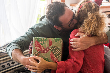 Man kissing woman at home and give her a christmas gift. Sharing xmas present concept leisure...