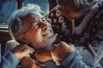 Portrait of couple of senior people in love at home in the evening dark light. Old man smile at her...
