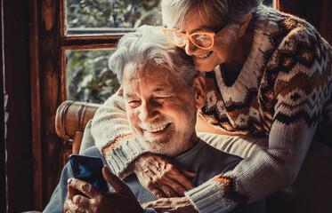 Happy senior old couple use mobile phone at home together to video call parents. Winter season...