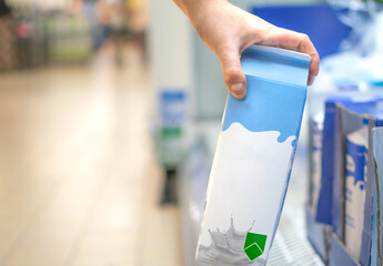 Hand taking a milk carton from supermarket shelf ready for consumption