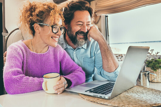 Man And Woman Using Laptop Inside Camper Van During Travel Lifestyle Van Life. Happy Couple Smile In Front Of A Computer During Rv Motor Home Vacation. Smart Working And Digital Nomad Concept Day