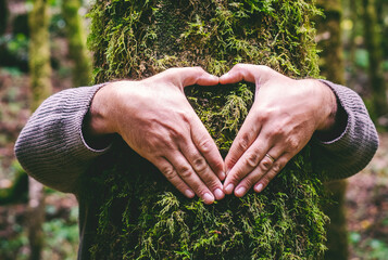 One man hugging a green tree trunk doing heart gesture with hands. People and love respect for nature forest and environment lifestyle. Environmentalist embrace trunk with musk. Stop climate change - obrazy, fototapety, plakaty