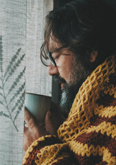 One man drinking hot drink at home covered with woolen cover. Concept of cold temperature at home...