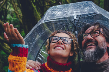 One couple have fun and enjoy bad weather rain under a transparent umbrella smiling together and...